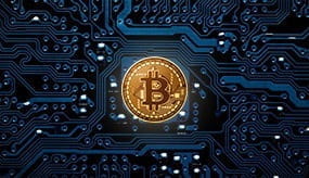 The bitcoin currency represented as a gold coin mounted to a computer circuit board